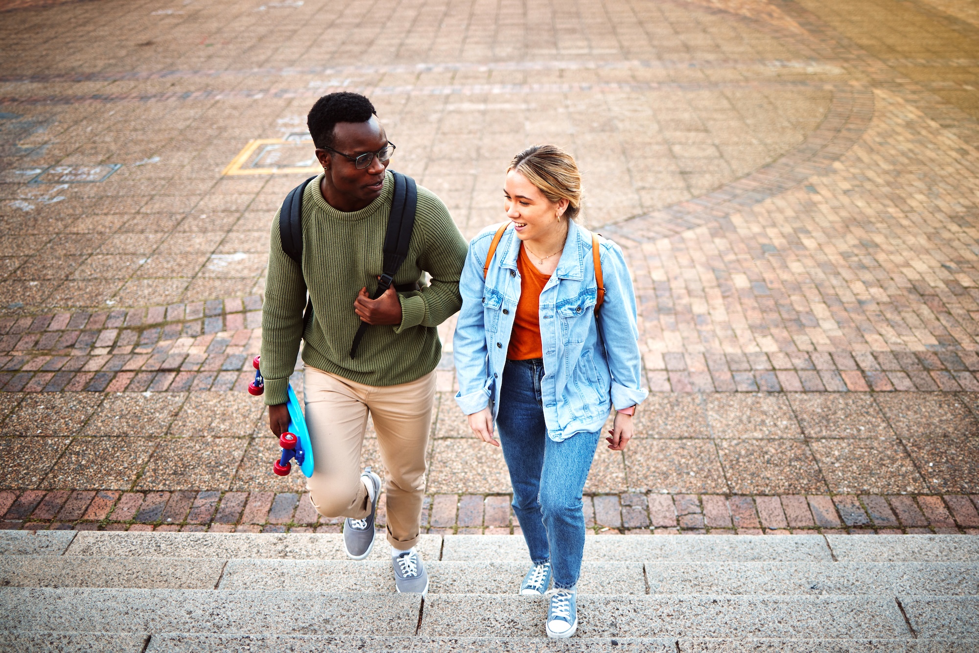 A young adult male and female walking up steps while talking to each other