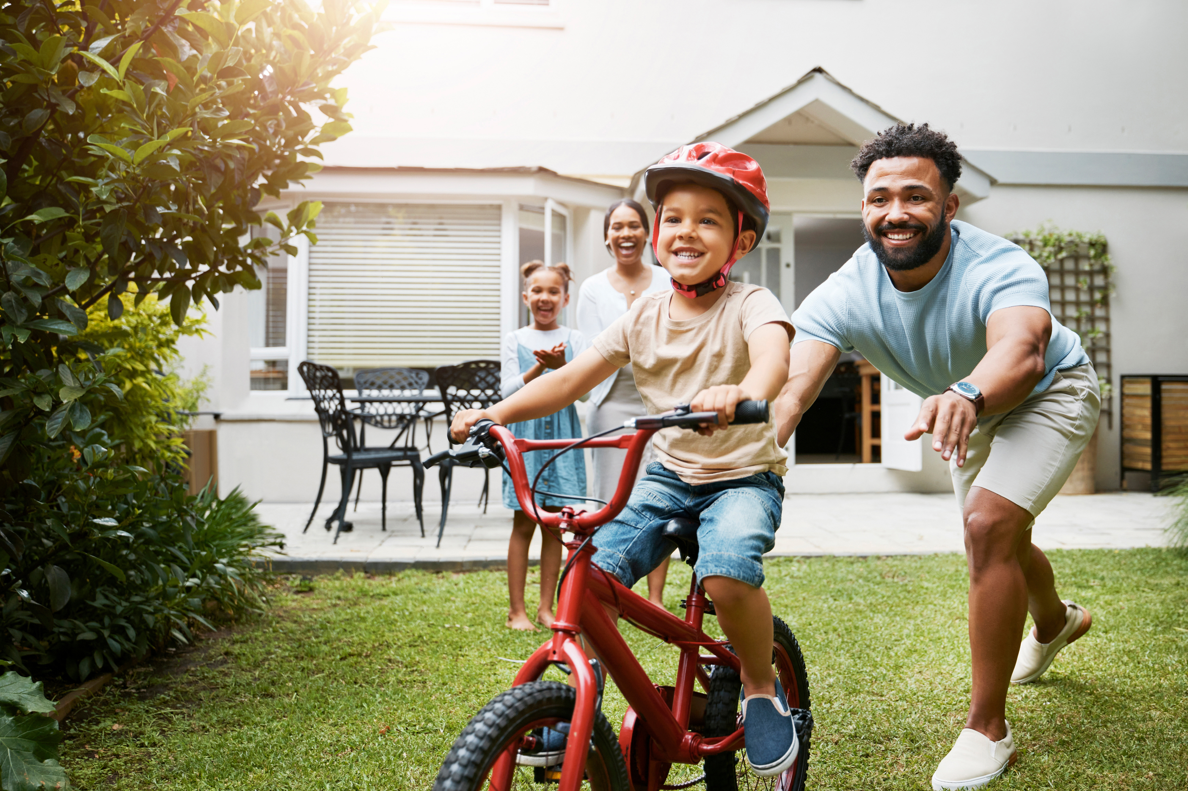 A family cheering as the father teaches his son how to ride a bike outdoors