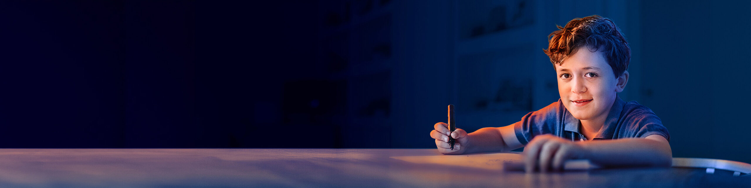 A young boy writing at his desk and smiling