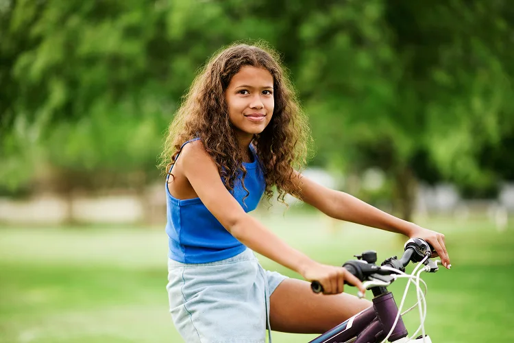 A young girl holding the handlebars on her bicycle and smiling