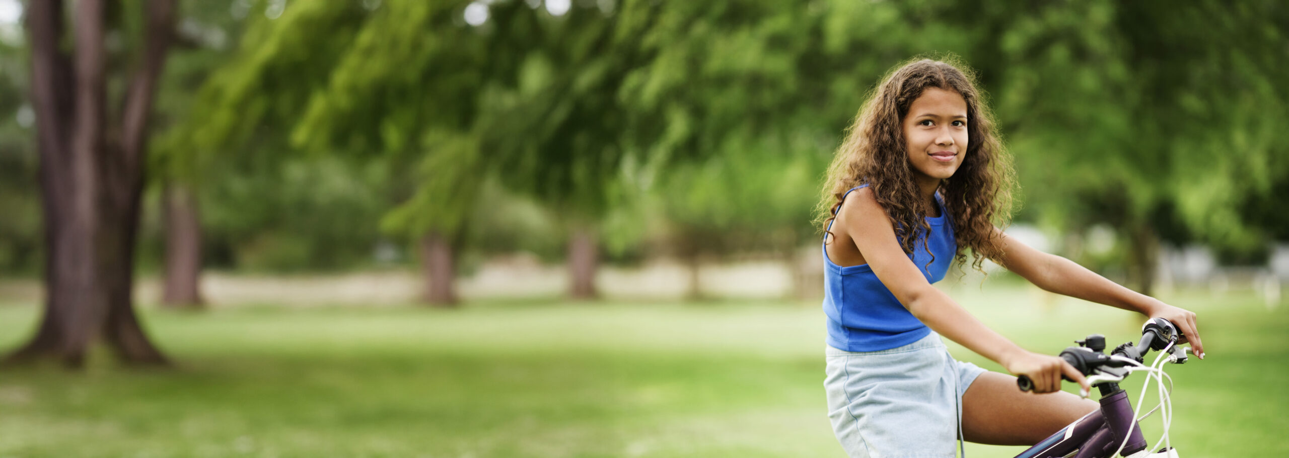 A young girl holding the handlebars on her bicycle and smiling
