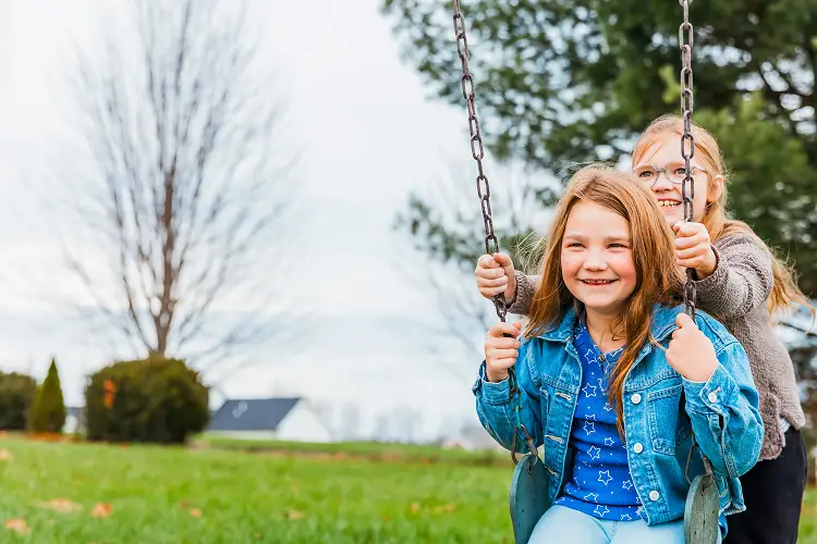 A young girl smiling while being pushed on a swing by her friend outdoors